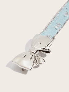 Macro shot of silver metal bow buckle on light blue denim belt with bead chain trim