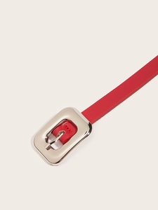 Gros plan sur une fine ceinture en cuir rouge avec une boucle ardillon argentée arrondie