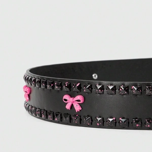Punk black leather belt with pink splatter studs and 3D bow decoration on grey background