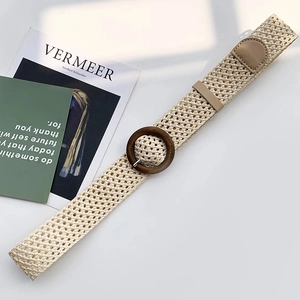 Detail of woven straw belt featuring a round wooden buckle and brown leather end tip