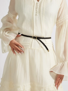 Detail of a thin black woven belt with a gold buckle on an elegant cream pleated dress