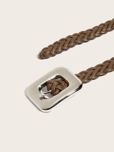 Détail d'une ceinture tressée marron avec une grande boucle carrée en argent sur fond beige