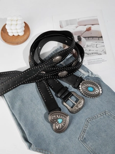 Tre cinture punk nere con borchie e fibbie turchesi su jeans in denim blu