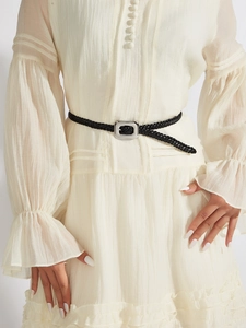 Détail d'une fine ceinture tressée noire sur une robe en mousseline plissée blanc cassé