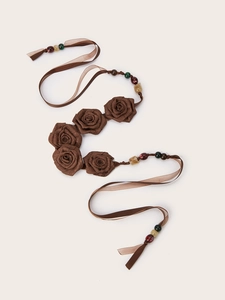 Dettaglio di rose in tessuto marrone fatte a mano e perline colorate su cintura boho
