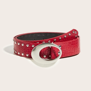 Macro shot of a red embossed belt with silver oval buckle and metal rivets decoration