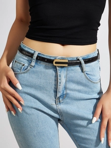 Detail of thin black crocodile-textured belt with gold C-buckle on light blue denim jeans