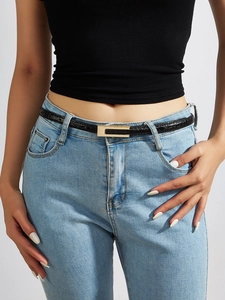 Detail of slim black crocodile embossed leather belt with gold buckle on denim jeans