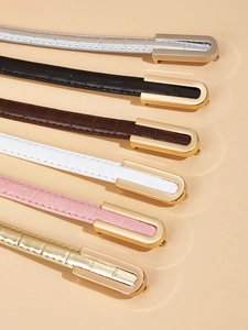 Detail of six narrow faux leather belts with crocodile texture and metal U-shaped buckles