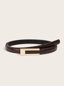 Detail of slim dark brown belt with crocodile pattern and minimalist gold buckle