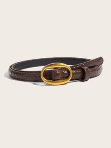Close-up of thin brown leather belt with crocodile texture and oval bronze buckle