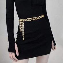 Detail of gold metal waist chain with ring links and leaf pendant on black dress