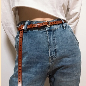 Detail of brown leather belt with heart-shaped cutouts styled on denim jeans