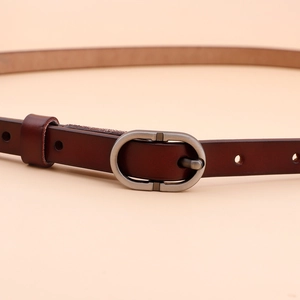 Women's dark brown slim leather belt featuring a matte silver oval buckle on beige backdrop