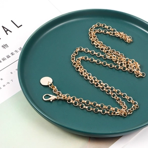 Nahaufnahme einer goldenen Metall-Taillenkette mit Karabiner auf grünem Keramikteller