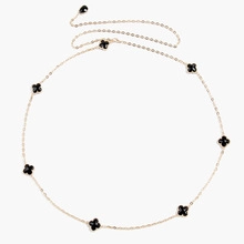 Detail of a gold-tone chain belt with seven black clover charms on a white background