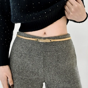 Detail of a minimalist gold metal elastic belt with a rectangular polished buckle on a model