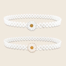 Detail of two white pearl headbands featuring enamel daisy flower decorations on beige