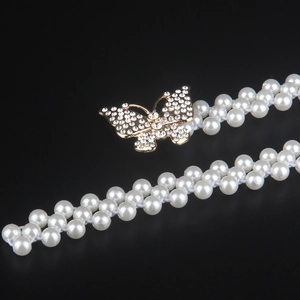 Close-up of bow-shaped rhinestone buckle and double-row pearl elastic belt on black background