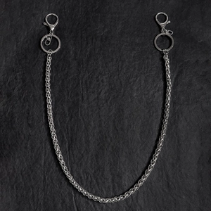 Dettaglio catena per pantaloni in metallo argento con moschettone su sfondo di pietra scura