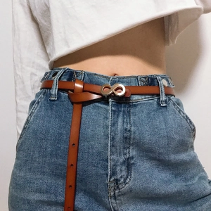 Close-up of a brown leather belt with a golden infinity metal buckle on jeans