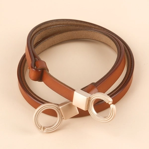 Detail of thin brown leather belt featuring carved golden double C-ring metal buckle