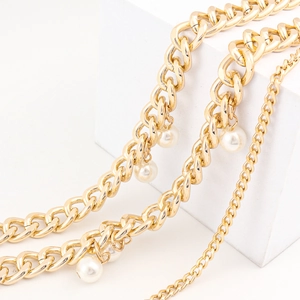 Multi-layered gold metal chain belt with pearl accents displayed on minimalist white props
