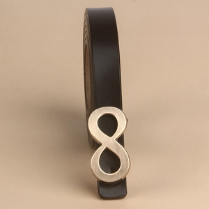 Detail of matte gold infinity buckle on black leather belt with brushed metal texture