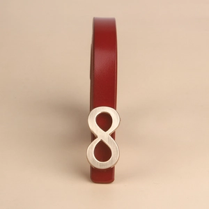 Close-up of slim red leather belt with brushed gold infinity buckle on beige background