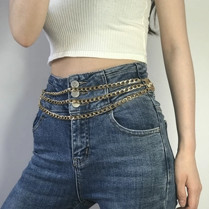 Détail d'une élégante chaîne de taille multicouche en aluminium doré sur un jean bleu