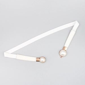 Détail de la ceinture élastique blanche avec boucle en métal doré et perle élégante