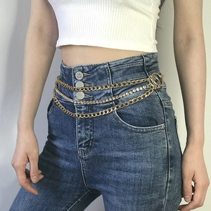 Detail of layered gold hip chain with rhinestones on white top and denim jeans