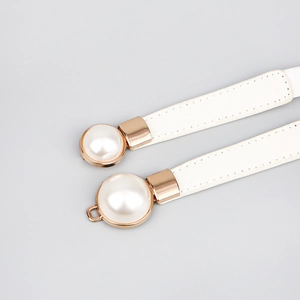 Détail de ceinture fine en cuir blanc avec boucle dorée champagne et perle élégante