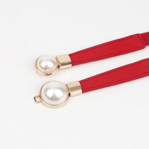 Détail d'une ceinture élastique rouge avec grosse perle et boucle en métal doré chic