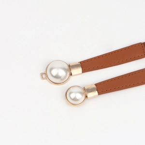Détail de ceinture fine en cuir marron avec boucle dorée et accents de perles blanches