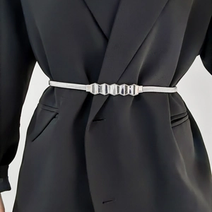 Close-up of slim silver elastic snake chain belt with geometric buckle on black blazer