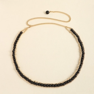 Close-up of golden metal chain belt featuring elegant black circular bead accents