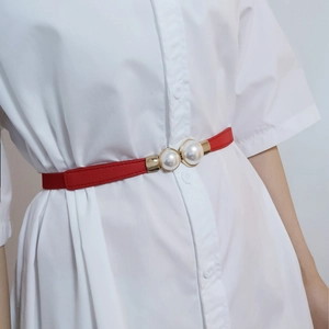 Détail de la fine ceinture rouge avec boucle double perle sur une robe blanche