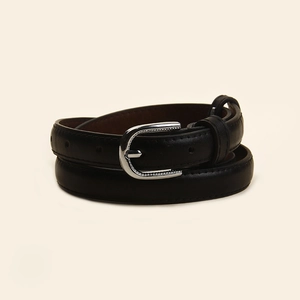 Détail d'une fine ceinture en cuir noir avec boucle fer à cheval argentée et coutures précises