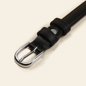 Détail d'une fine ceinture en cuir noir avec une boucle ovale en argent et des coutures
