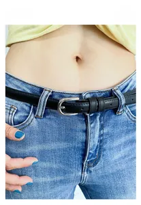 Détail d'une fine ceinture en cuir noir avec boucle argentée ajourée sur un jean