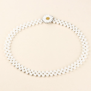 Détail d'une chaîne de taille en perles à deux rangs avec breloque marguerite sur fond beige