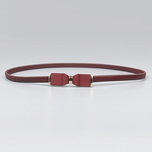 Détail d'une ceinture élastique bordeaux fine avec une boucle dorée en forme de nœud chic