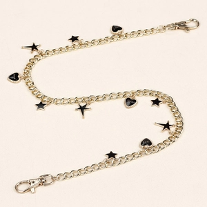 Detail of gold metal pant chain featuring black enamel heart and star shaped charms