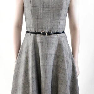 Détail d'une fine ceinture noire vernie avec boucle nœud dorée sur robe à carreaux