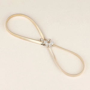 Dettaglio cintura elastica in metallo dorato con fibbie a doppia farfalla e strass lucenti