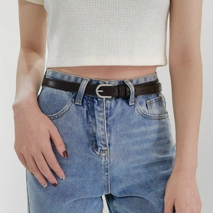 Détail d'une ceinture fine en cuir marron foncé avec boucle fer à cheval sur un jean bleu