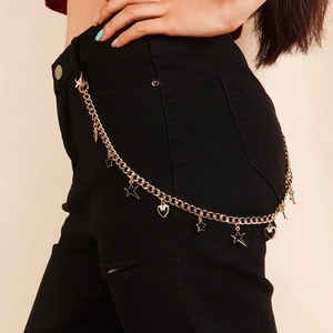 Detail of gold pant chain with hollow stars and black heart pendants on denim jeans