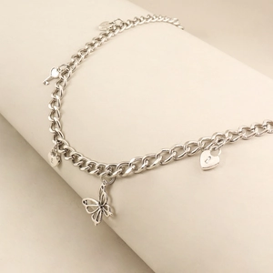 Silberne Metallkette mit Schmetterlingsanhänger und Herzschloss-Charms auf weißem Ständer