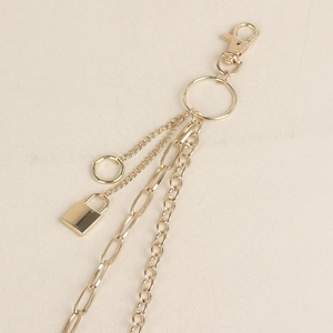 Detail view of multi-layered golden metal pant chains with a square lock and ring pendant